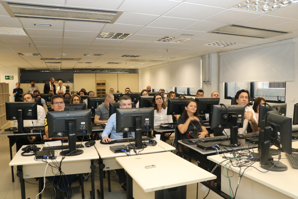 Imagem colorida de várias pessoas olhando para a tela de computadores em um treinamento sobre o sistema EPROC.